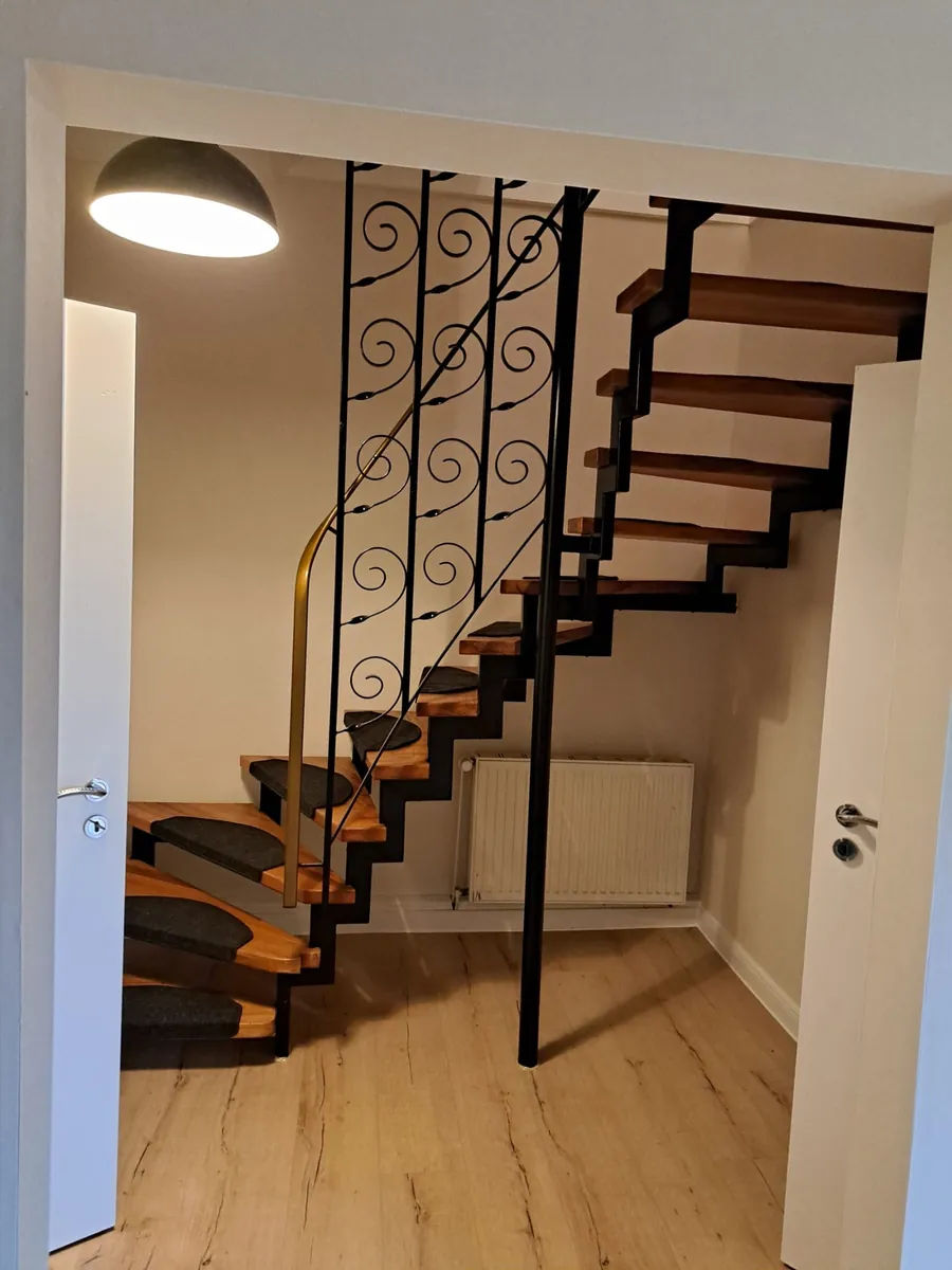 Sanierte Treppe mit neuen Holzstufen und schmiedeeisernem Geländer, daneben frisch verlegter Dielenboden